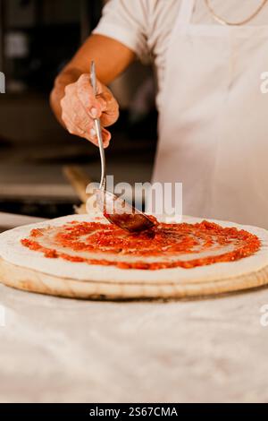 Man fügt Sauce zu Pizza hinzu Stockfoto