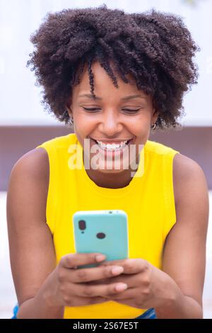 Lächelnde afroamerikanische junge Frau, die draußen ein Smartphone hält. Vertikal Stockfoto