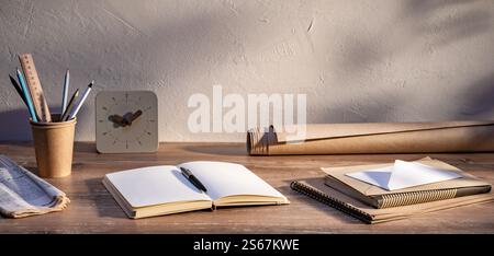Schreibtisch mit Notebooks, Schreibgeräten und Korrespondenz bei Sonnenlicht tagsüber Stockfoto