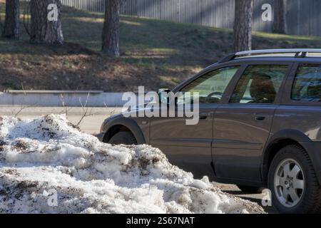 Dunkelgraues Crossover auf einer verschneiten Straße vorbei an Bäumen. Stockfoto