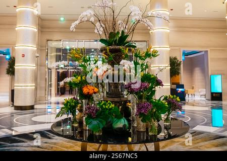 Elegante Blumenarrangements mit leuchtenden lila Orchideen und üppig grünen Blättern in goldenen Töpfen auf Marmoroberfläche in der luxuriösen Hotellobby. Abu Dhabi. . Hoch Stockfoto