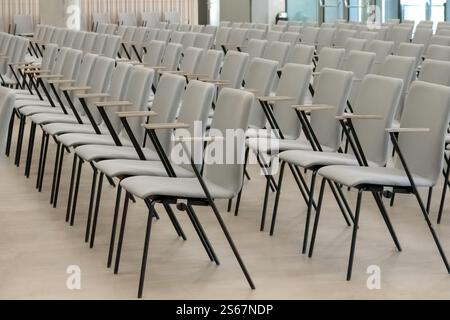 Ein leeres Fragment eines Konferenzsaals oder Auditoriums mit Reihen grauer Stühle mit Holzarmen. Stockfoto