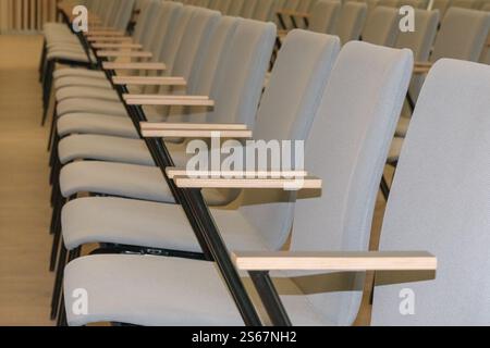 Ein leeres Fragment eines Konferenzsaals oder Auditoriums mit Reihen grauer Stühle mit Holzarmen. Stockfoto