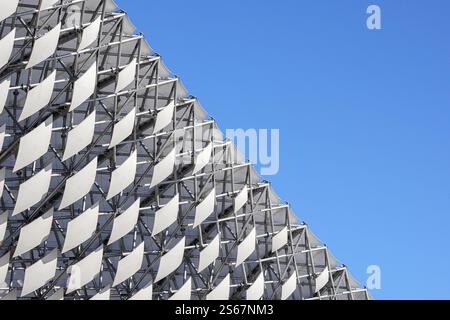 Ein Fragment moderner Architektur – ein Raster aus weißen, diamantförmigen Paneelen, die eine große, abstrakte Oberfläche am Himmel bilden. Stockfoto