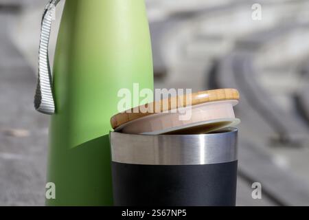 Eine Thermoskanne aus Edelstahl mit schwarzer Beschichtung und einem Bambusdeckel neben einer größeren grünen Thermoskanne mit Griff. Stockfoto