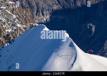 Ein schneebedeckter Berggipfel mit einem Gleitschirmflieger, der in eine tiefe Schlucht hinaufsteigt, die zum Mer de Glace in Chamonix führt, von Aiguille du Midi aus gesehen. A bre Stockfoto