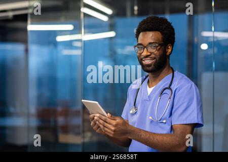 Porträt eines erfolgreichen Arztes mit einem Tablet-Computer in den Händen, Mann lächelt und in die Kamera blickt. Der Arzt ist im Büro der modernen Klinik, arbeitet abends und berät Patienten aus der Ferne. Stockfoto