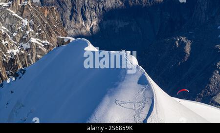 Ein schneebedeckter Berggipfel mit einem Gleitschirmflieger, der in eine tiefe Schlucht hinaufsteigt, die zum Mer de Glace in Chamonix führt, von Aiguille du Midi aus gesehen. A bre Stockfoto