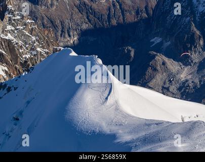 Ein schneebedeckter Berggipfel mit einem Gleitschirmflieger, der in eine tiefe Schlucht hinaufsteigt, die zum Mer de Glace in Chamonix führt, von Aiguille du Midi aus gesehen. A bre Stockfoto