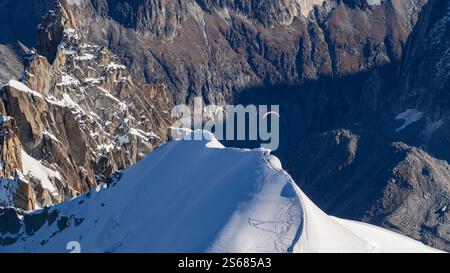 Ein schneebedeckter Berggipfel mit einem Gleitschirmflieger, der in eine tiefe Schlucht hinaufsteigt, die zum Mer de Glace in Chamonix führt, von Aiguille du Midi aus gesehen. A bre Stockfoto