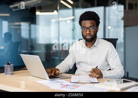 Porträt eines erfolgreichen, seriösen Buchhalters am Arbeitsplatz, Mann, der fokussiert auf die Kamera blickt. Geschäftsmann, der im Büro Papierkram macht, mit Verträgen und Berichten arbeitet, Dokumente. Stockfoto