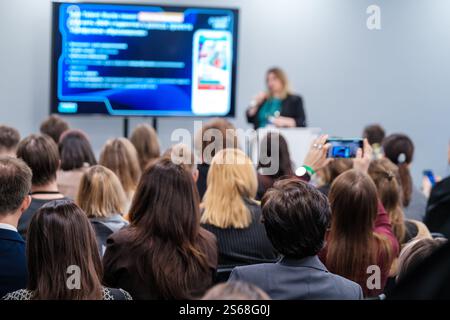 Personen, die an einer Konferenz teilnehmen, hören einem Sprecher mit sichtbarem Präsentationsbildschirm zu. Geschäfts- und Netzwerkfokus. Stockfoto