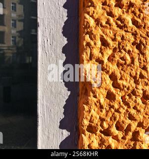 Detaillierte Ansicht einer leuchtend orange strukturierten Wandoberfläche im Kontrast zu den Schatten im Sonnenlicht. Mit architektonischen Details. Stockfoto