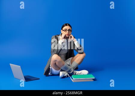 Eine junge Frau drückt tiefe Emotionen aus, während sie auf dem Boden sitzt, umgeben von Büchern und einem Laptop. Stockfoto