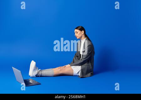 Eine junge Frau drückt ihre Gefühle aus, während sie auf dem Boden sitzt und mit ihrem Laptop beschäftigt ist. Stockfoto