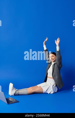 Eine schöne junge Frau drückt ihre Begeisterung aus, indem sie ihre Arme hochhebt und stilvoll gekleidet ist. Stockfoto