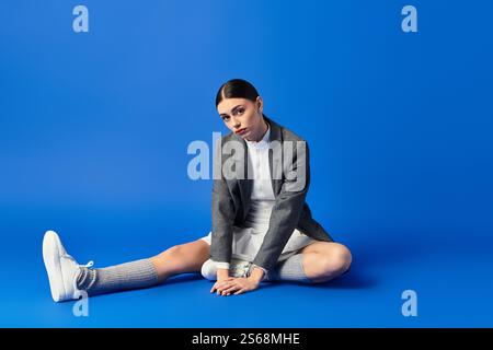 Eine schöne junge Frau drückt ihre Gefühle aus, während sie auf einem hellblauen Hintergrund sitzt. Stockfoto