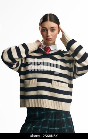 Eine schöne junge Frau drückt ihre Emotionen in einem stilvollen gestreiften Pullover und einem karierten Rock aus. Stockfoto