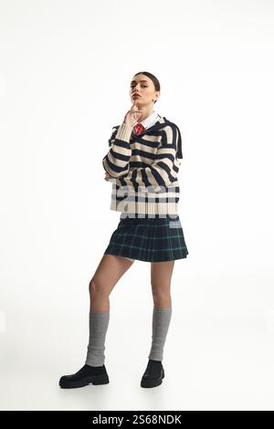 Die schöne Frau steht selbstbewusst und trägt ein trendiges Outfit mit reflektierendem Ausdruck. Stockfoto