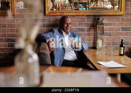 Ein elegant gekleideter schwarzer Geschäftsmann, der sich mit seinem Lieblingsgetränk in einer trendigen Bar entspannt. Stockfoto