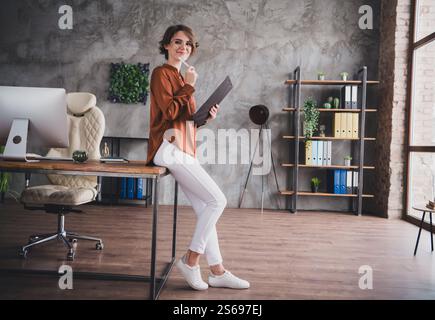 Foto in voller Länge von einer netten jungen Dame gelesen Bericht gekleidet mit braunem Satin Hemd Startup Büroraum Innenraum Stockfoto