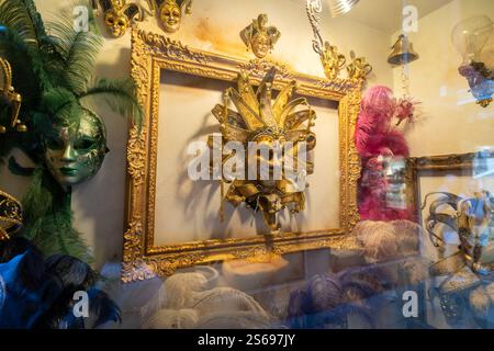 Eine lebendige Ausstellung venezianischer Karnevalsmasken mit goldenen, grünen und rosa Motiven, die mit Federn und komplizierten Details in einem Schaufenster verziert sind. Stockfoto