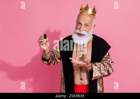 Porträt des alten Mannes Theaterschauspieler tragen Leopardenmantel Krone zeigen goldenes Handy isoliert auf rosa Hintergrund Stockfoto