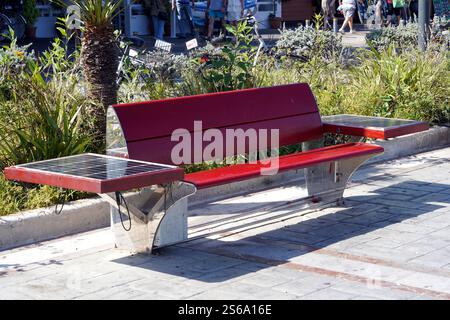 Eine rote Holzbank mit Solar-Photovoltaik-Panels zum Laden von Mobiltelefonen. Stockfoto