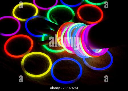 Mädchen Handgelenk mit Regenbogenarmbändern. Neonlicht leuchtet im Dunkeln Stockfoto