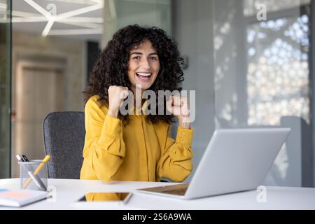 Erfolgreiche Geschäftsfrau am Arbeitsplatz lächelnd und mit der Kamera in der Hand. Frau feiert Sieg siegreiche Ergebnisse am Arbeitsplatz im Büro. Stockfoto