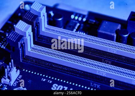 Nahaufnahme der RAM-Steckplätze auf einem Motherboard unter blauer Beleuchtung, mit den Steckplätzen für Speichermodule und den komplizierten Details der Leiterplatte. Perfec Stockfoto