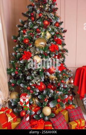 Ein lebendiger Weihnachtsbaum mit festlichen Ornamenten und Girlanden steht in einem gemütlichen Raum. Bunte Geschenke sind ordentlich unter dem Baum angeordnet, Creat Stockfoto