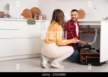 Junge Frau und Klempner reparieren Spülbecken in der Küche Stockfoto