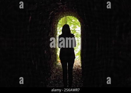 Silhouette einer Frau, die in einem dunklen Tunnel in einem Wald steht - aufgenommen in Lake District, Cumbria, England, Großbritannien Stockfoto