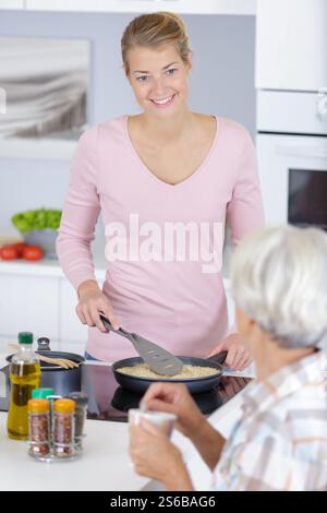 Junge Frau, die in der Küche für Mutter kocht Stockfoto