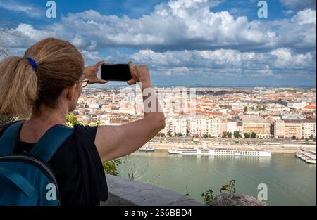 Budapest, Ungarn, 29. August 2022. Eine Frau mittleren Alters fotografiert mit ihrem Handy die herrliche Stadtlandschaft von der Spitze des Hügels. Beau Stockfoto