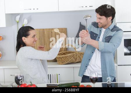 Komisches Paar, das sich in der Küche mit Utensilien streitet Stockfoto