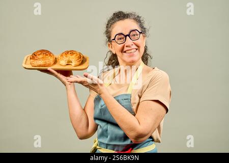 Lächelnde Bäckerin zeigt und präsentiert zwei frisch gebackene Brötchen mit einem Biss aus einem davon Stockfoto