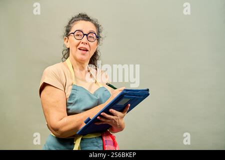 Eine Frau in einer blauen Schürze hält ein Klemmbrett und lächelt Stockfoto