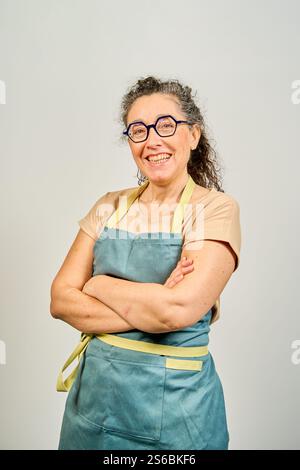Eine Frau mit blauer Schürze und Brille lächelt. Sie trägt eine gelbe Schürze und hat die Arme gekreuzt Stockfoto