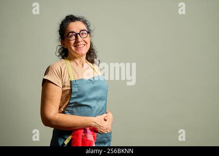 Eine Frau mit blauer Schürze und Brille steht vor einer weißen Wand Stockfoto