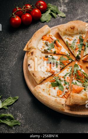 Geschnittene Gourmet-Pizza mit Räucherlachs, Rucola und Kapern auf einem rustikalen Holzbrett Stockfoto
