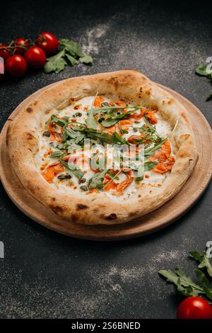 Gourmet-Pizza mit Räucherlachs, Rucola und Kapern auf einem Holzbrett für eine köstliche Mahlzeit Stockfoto