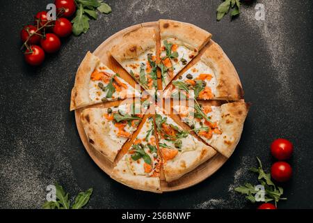 In Scheiben geschnittene Gourmet-Pizza mit Räucherlachs, Rucola und Kapern auf einem Holzbrett für ein stilvolles fest Stockfoto