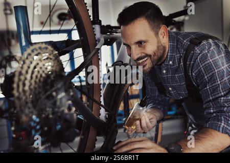 Porträt eines gutaussehenden lächelnden Reparaturmannes im Overall, der Reifenpumpe in der Werkstatt hält, mit Fahrrad im Hintergrund Stockfoto