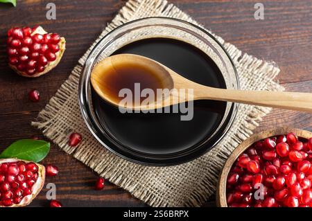 Granatapfelmelasse in Glasschale, Granatapfelsauersauce mit frisch reifer ganz und gespaltener Granatapfelfrucht auf rustikalem Holztisch (Punica granatum) Stockfoto
