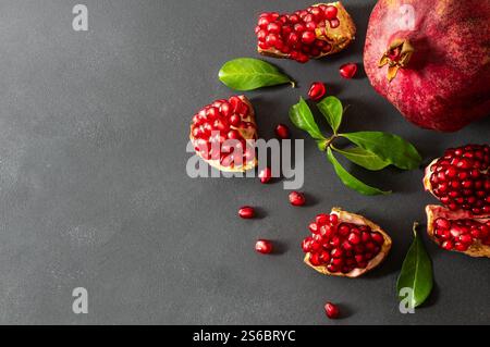 Frischer reifer ganzer und gespaltener saftiger Granatapfel mit Samen und Blättern auf rustikalem hölzernem Hintergrund, gesunde rote Früchte Konzept Kopierraum (Punica granatum Stockfoto