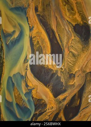 Aus der Vogelperspektive isländischer geflochtener Flüsse, die komplexe gelbe und blaue Muster schaffen, die abstrakten Kunstwerken auf der vulkanischen Landschaft ähneln. Stockfoto