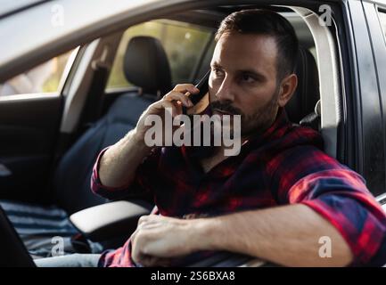 Hübsche junge Frau in kariertem Hemd, die Auto fährt und mit dem Handy spricht Stockfoto