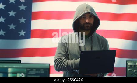 Ein Hacker, der in einem staatlichen IT-Arbeitsbereich arbeitet und die USA-Flagge auf einem großen Bildschirm zeigt. Gewährleistung der Cybersicherheit, der Analyse von Cyberbedrohungen und der globalen Überwachung zur Gewährleistung des Cyberschutzes. Kamera A.. Stockfoto